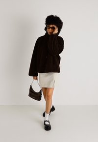 Hnedá kordová oversized bunda, smotanová mini sukňa, čierne platformové topánky, biele ponožky a malá čierna kabelka s reťazovým popruhom.