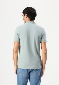 Kortermet polo-skjorte i lysegrønn stoff med en glatt tekstur. Har krage og sidelangt, kombinert med blå jeans.