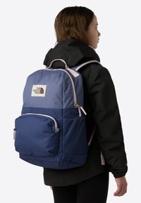 Blue and navy fabric backpack with pink accents, large main compartment, front pocket, and side mesh pocket, featuring a logo patch.