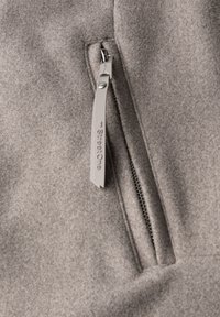 Tessuto feltro grigio con una texture liscia, caratterizzato da una cerniera argento e un tirante grigio con l'etichetta "StreetOne". Primo piano sulla tasca con cerniera.