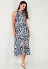 Navy blue maxi dress with white leaf pattern, sleeveless design, button details, side slit, lightweight fabric, and a flowy silhouette.