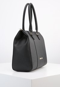 Czarna, strukturalna torebka z podwójnymi uchwytami i teksturowaną powierzchnią, umieszczona na białym pedestale na jednolitym tle.