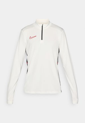 Haut de sport à manches longues blanc avec un col zippé quart, des accents noirs sur les côtés, et un logo Nike rouge sur la poitrine gauche.