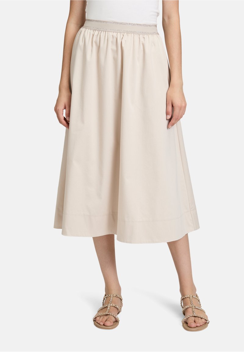 Jupe beige en coton, longueur genou, avec taille élastique et texture douce. Associée à des sandales plates à brides.