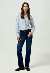 Sinine denimist valmistatud sirge lõikega teksad, mille juurde on kombineeritud helesinine triibuline nööpidega särk ja must vööd, kantud läikivate mustade kingadega.