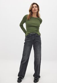 Green ribbed long-sleeve top paired with high-waisted, wide-leg gray denim jeans. The outfit is complemented by black glossy loafers.