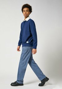 Granatowy sweter z białym kołnierzykiem, zestawiony z jasnoniebieskimi spodniami. Stylizacja ma luźny krój i subtelną metkę marki na swetrze.
