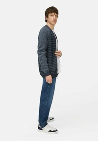 Sweter dziergany w ciemnoniebieskim kolorze z teksturowanym wzorem, noszony na białej koszulce. Jeansy w slim fit i białe buty z granatowymi akcentami.
