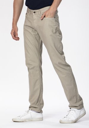 Pantalon en coton beige avec une coupe droite, doté de poches avant et d'une fermeture à bouton, associé à des baskets blanches décontractées.