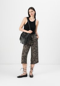 Top sans manches noir, pantalon court en imprimé léopard, sac bandoulière à franges noir, et ballerines noires à lacets. Tissu lisse avec une coupe décontractée.