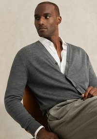 Gray cardigan with a v-neck, button front, and ribbed cuffs, worn over a white collared shirt and paired with gray trousers.