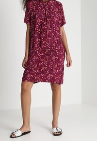 Magenta blomsterkjole med korte ærmer og krave, med rynkede detaljer. Kombineret med sorte og hvide flade sandaler.