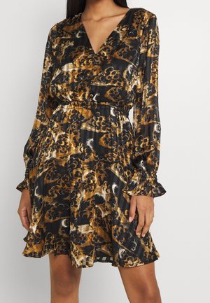 Woman wearing a long-sleeve, V-neck dress with a black, brown, and gold abstract floral pattern and an elastic waist.