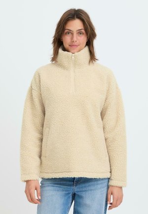 Pull en polaire beige avec un col montant, fermeture éclair à mi hauteur et tissu texturé. Présente une coupe décontractée et des manches longues.