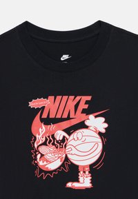 Μαύρο βαμβακερό t-shirt με μεγάλο κόκκινο λογότυπο της Nike και ένα καρτούν χαρακτήρα που κρατάει μια μπάλα του μπάσκετ με θέμα τη φωτιά και χαριτωμένες λεπτομέρειες.