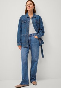 Giubbotto di jeans con taglio classico, due tasche sul petto e maniche larghe, abbinato a jeans svasati di un blu chiaro e ballerine a punta color nude.