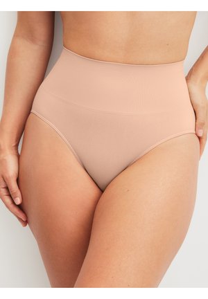 Model draagt naadloze shapewear slips in een naaktkleur met hoge taille, toont de taille en bovenbenen tegen een effen achtergrond.