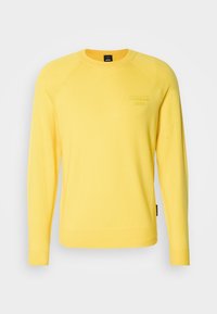 Pull jaune à manches longues avec col rond, orné d'un logo discret "Porsche BOSS" embossé sur la poitrine gauche, présenté sur un fond clair uni.
