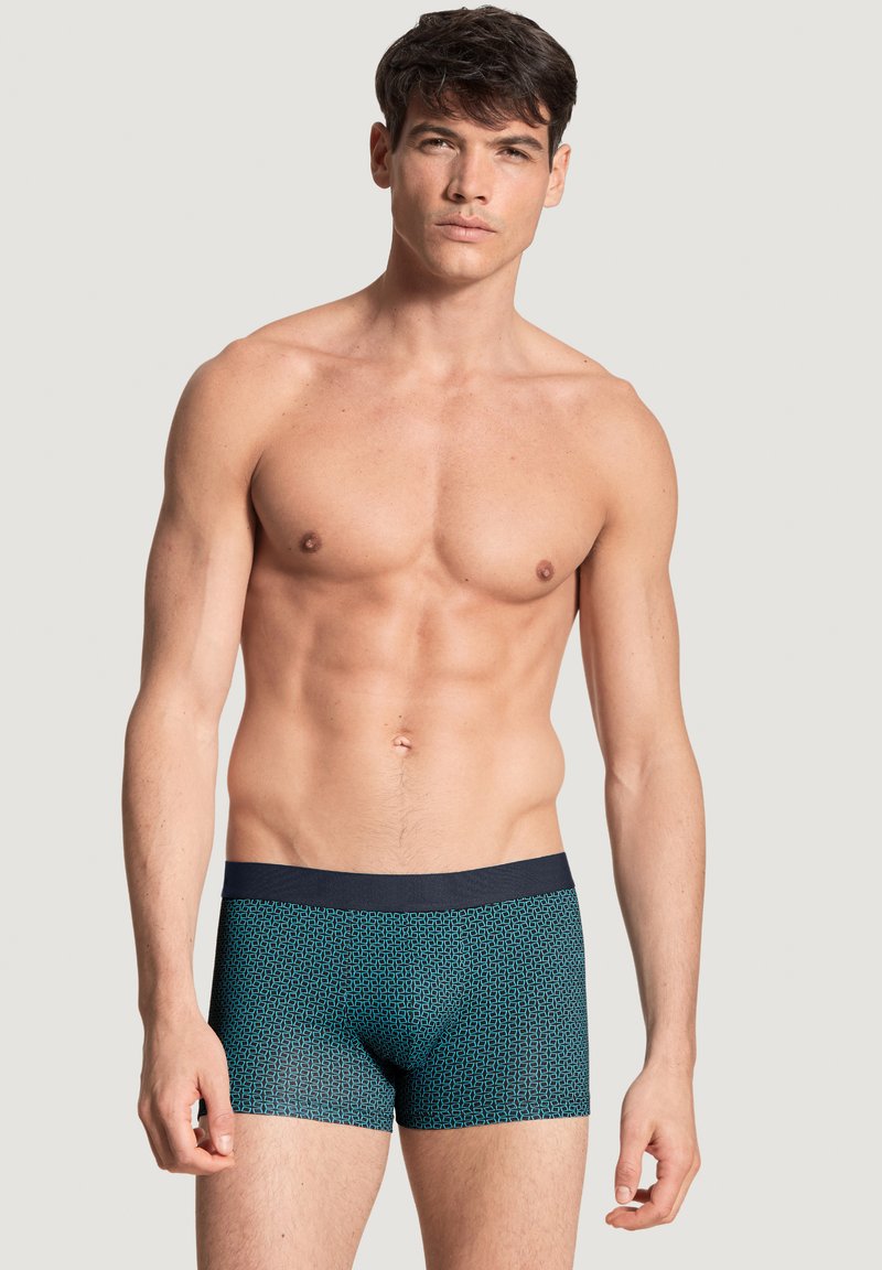 Heren trunks ondergoed in een blauw geometrisch patroon met een donkere tailleband. Gemaakt van zachte stof, met een getailleerd ontwerp en een gladde textuur.