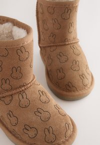 Braune Wildleder-Stiefeletten mit einem wiederholten Hasengesichtsmuster, Kunstpelzfutter und sichtbaren Nähten entlang der Nähte.