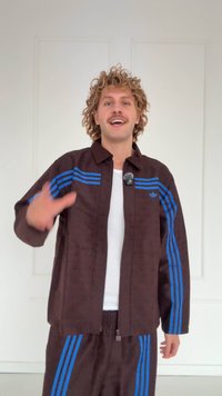 Bruine sportieve trainingspak met blauwe strepen, bestaande uit een gevoerd jack met rits en bijpassende broek. De stof lijkt glad met een subtiel patroon.