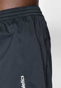 Black athletic shorts made of textured fabric, featuring an elastic waistband and a white printed logo on the side.