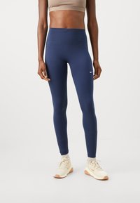 Marineblå leggings med høy midje, laget av elastisk stoff, med en liten hvit Nike-logo på venstre hofte. Lett design.