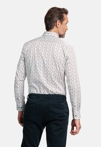 Witte shirt met een klein, multicolored vierkant patroon, lange mouwen en knoopmanchetten. Donkere broeken met achterzakken, van achteren getoond.