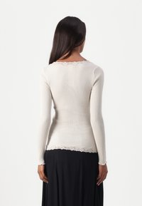 Beige ribbed long-sleeve top with delicate lace trim along the neckline and hem, featuring a tailored fit and soft texture.