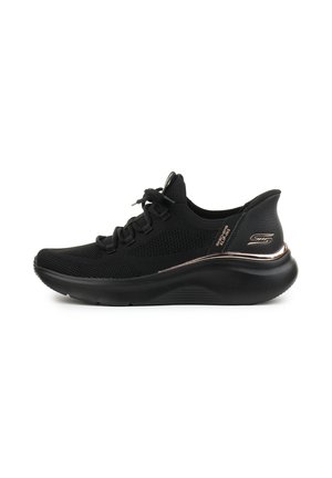 Chaussure de sport noire avec une tige en mesh, bout arrondi, semelle texturée et un accent doré brillant au niveau du talon. Présente un laçage standard.