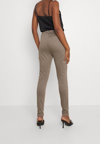 Bruine geruiten broek met een getailleerde pasvorm, hoge taille en een glanzende textuur, gecombineerd met zwarte hoge hakken en een zwart topje.