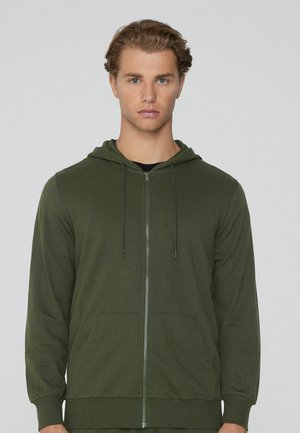 Sudadera verde con cremallera y bolsillo frontal, capucha con cordón y puños de canalé. Fabricada con una tela suave y de textura lisa.