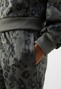 Leopardmønstret treningsdress i grått og svart med ribbet midjebånd og ermer. Har en sidelomme og adidas-logo.