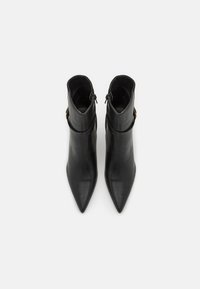 Bottes en cuir noir à cheville avec un bout pointu, dotées d'une fermeture éclair et d'un accent décoratif en métal doré près du col.