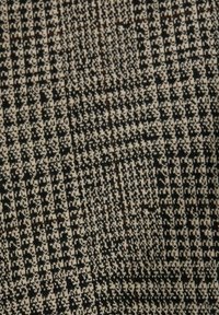 Stickad tyg med ett svart och beige houndstooth-mönster, med texturerade rutor och subtila inslag av brunt för djup.