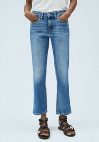 Jeans de mezclilla en azul claro con corte recto, que cuentan con bolsillos frontales, cierre de botón y dobladillo deshilachado. Combinados con sandalias negras.