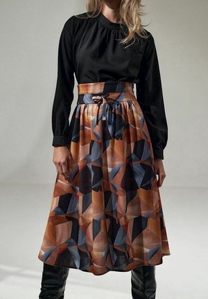 Haut noir à manches longues associé à une jupe longue au genou avec un motif géométrique dans des tons de marron, d'orange et de bleu, avec une ceinture assortie.