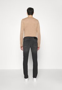 Světlohnědý top s dlouhým rukávem a detaily švů na zádech, doplněný tmavě šedými džíny s rovnými nohavicemi a bočním prošitím. Celý outfit završují bílé tenisky.