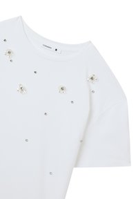 Maglietta bianca a maniche corte, con decorazioni floreali e piccoli strass sparsi sul davanti. Etichetta visibile all'interno del colletto.