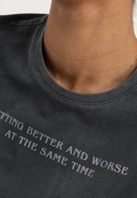 Grå kortærmet t-shirt med rund hals, der har trykt teksten "SITTING BETTER AND WORSE AT THE SAME TIME" i lys grå.
