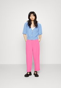 Cardigã azul curto de malha com mangas bufantes curtas, fecho de botão, combinado com calças largas cor-de-rosa e sapatos de plataforma pretos.