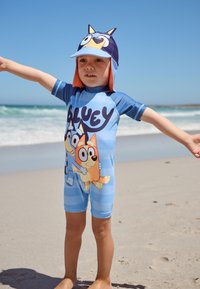Blauer Kinder-UV-Schutzanzug mit einem Cartoon-Design von Figuren auf einem hellblau gestreiften Hintergrund, kombiniert mit einer passenden Mütze.