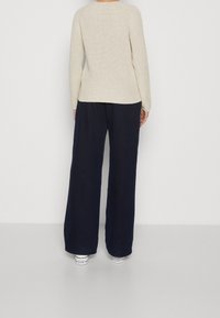 Beige geribbelde trui met lange mouwen, gecombineerd met donkerblauwe wijde broek en witte sneakers, gezien vanaf de achterkant.