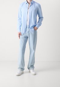 Camisa azul claro abotonada, camiseta blanca debajo, vaqueros azul claro y zapatillas blancas. Corte relajado con texturas suaves y diseño clásico.