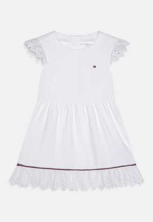 Vestido blanco de manga corta con detalles de encaje, falda recogida y pequeño logo en el pecho. Presenta un detalle de ojales florales a lo largo del dobladillo.