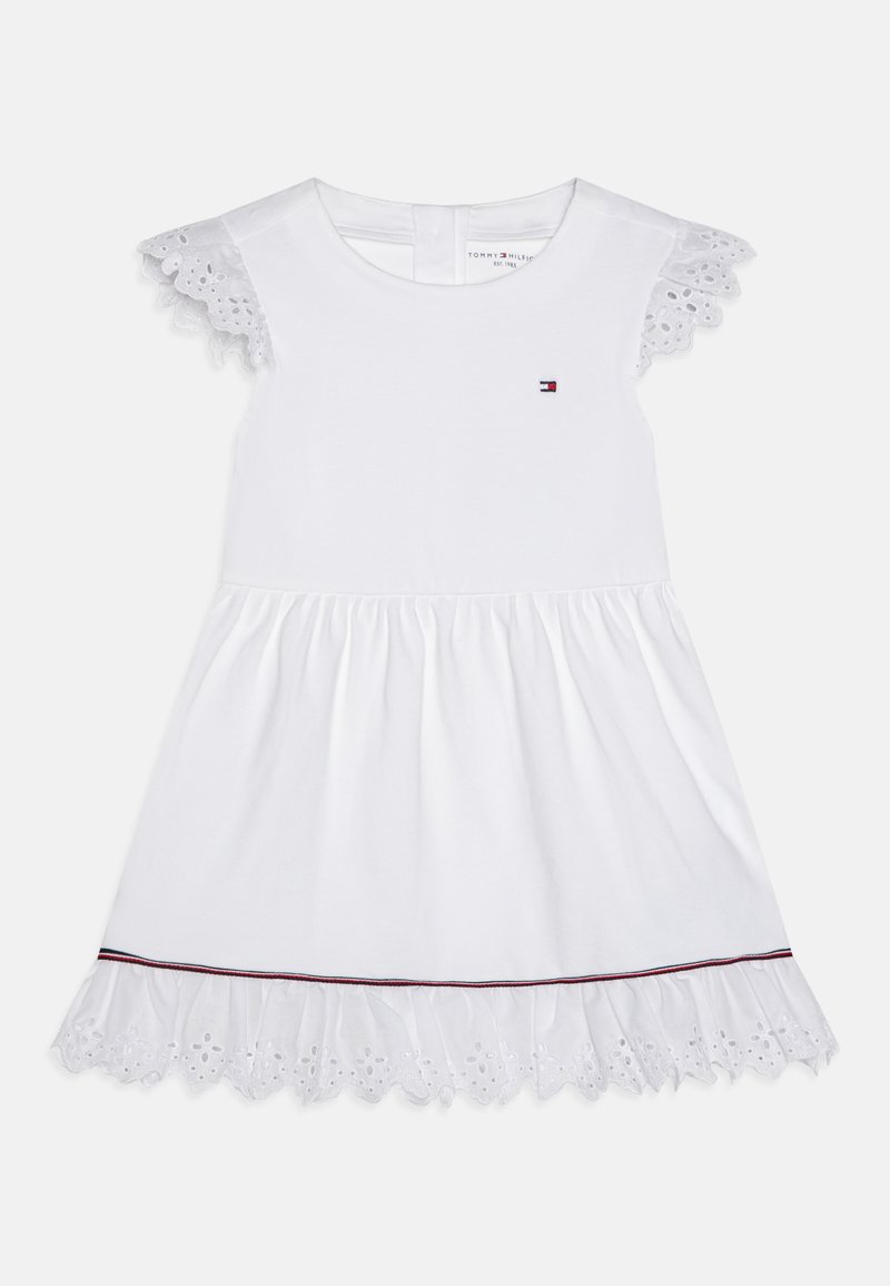 Bijela haljina kratkih rukava s čipkastim rubom, skupljenom suknjom i malim logotipom na prsima. Ima cvjetni otvoreni uzorak duž obruba.