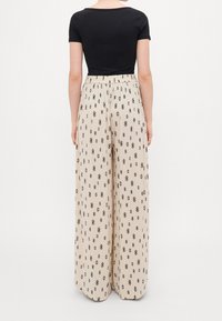 Haut noir ajusté associé à un pantalon beige à jambes larges présentant un motif en losange noir et une texture subtile. Taille élastique pour le confort.