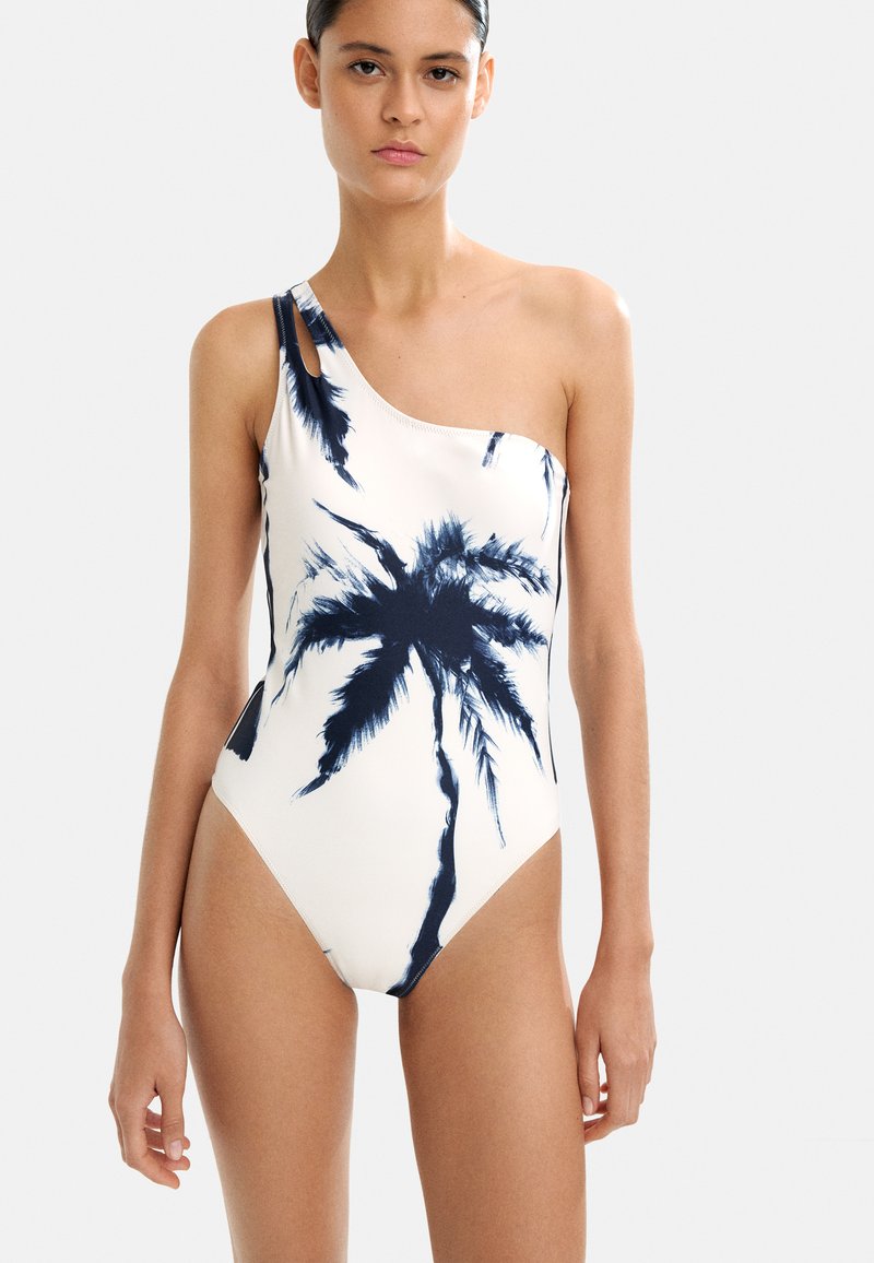 Jedno-boczny strój kąpielowy w kremowej bieli z nadrukiem palm w granatowym kolorze. Gładki materiał, dopasowany krój oraz wycięcie na ramieniu.