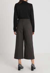 Černý top s dlouhým rukávem v kombinaci se širokými šedými kostkovanými kalhotami a botami na podpatku s puntíky. Viditelné švy a kapsy na kalhotách.