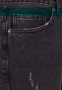 Zwarte denim jeans met een versleten textuur, voorzien van een groene tailleband en subtiele stiksels. Inclusief een klein voorvakje.